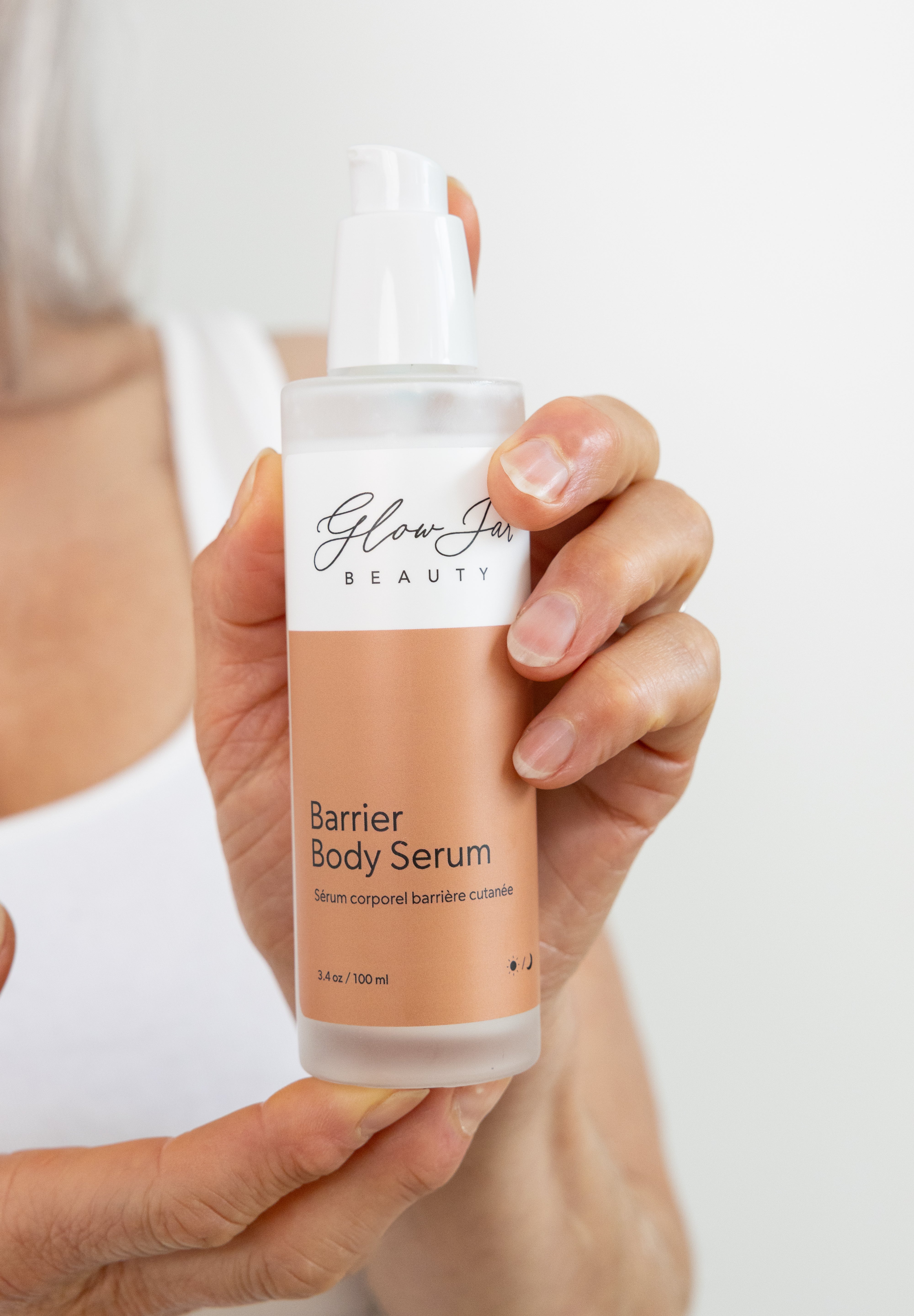 Hand holding a bottle of Glow Skin Beauty Barrier Body Serum against a neutral background