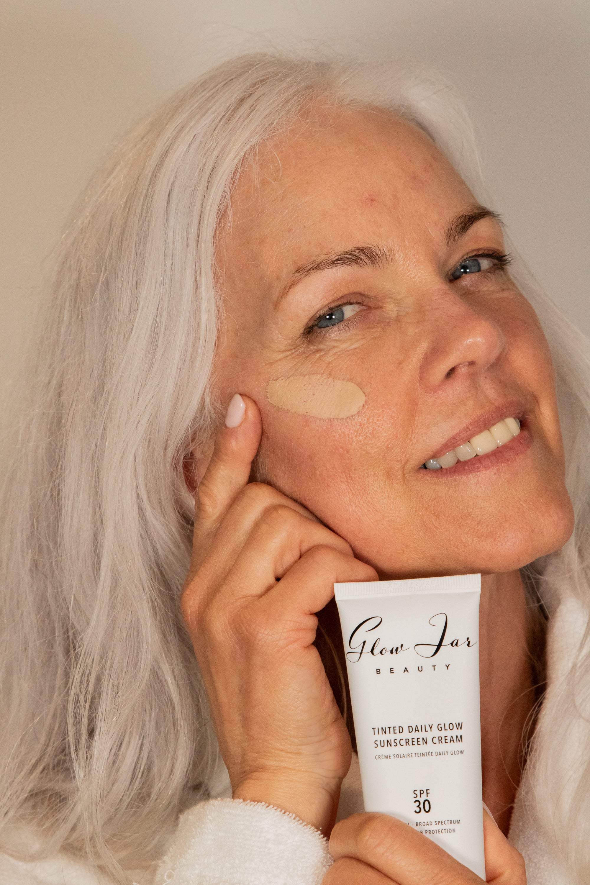 Woman applying sunscreen cream to her face with a product labeled 'Glow Jar Beauty' in the foreground.