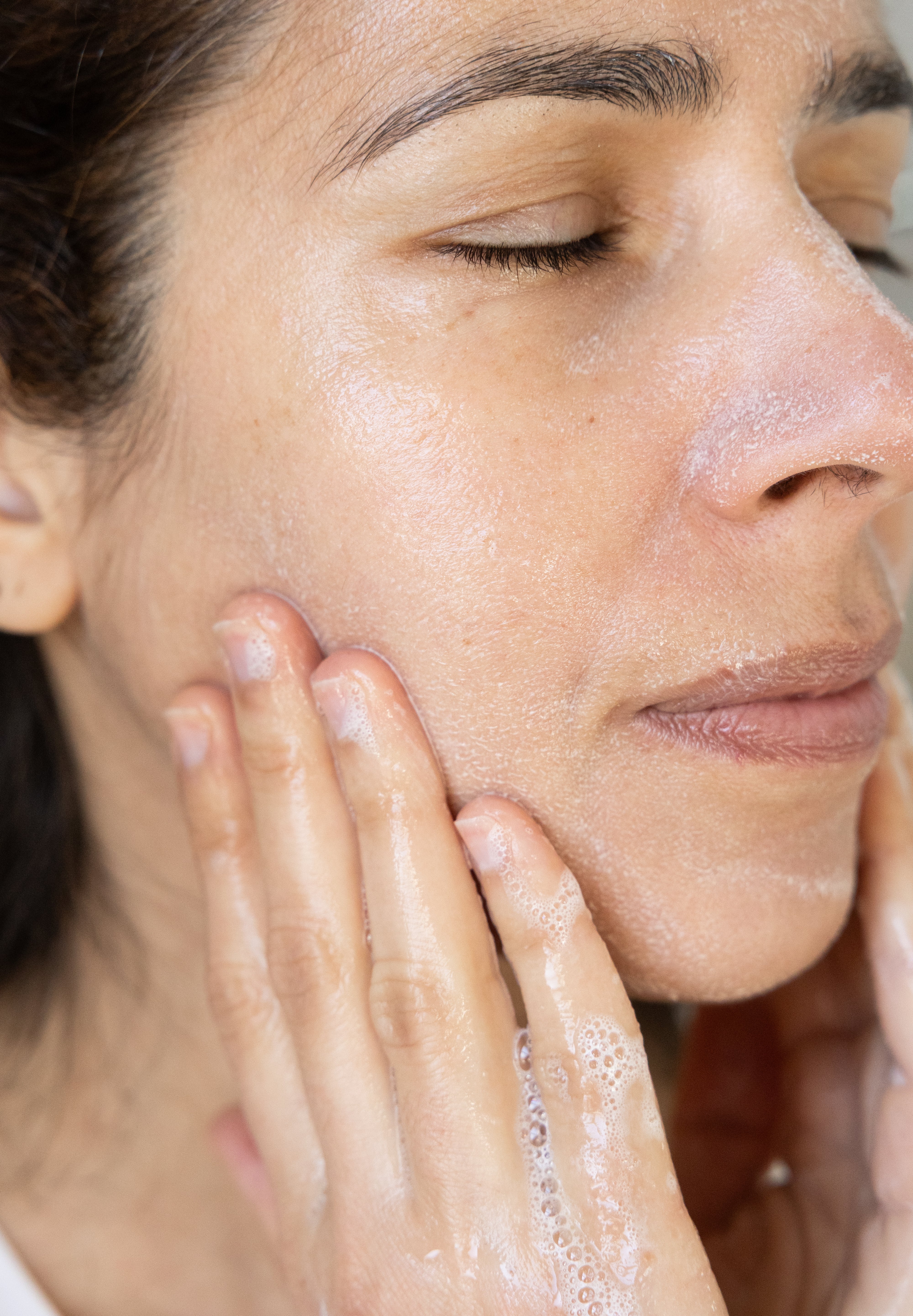 Woman applying a gentle gel cleanser to her face with her hands.