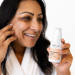 A woman holds up a bottle of Glow jar Beauty 8% Vitamin C Serum, smiling and touching her cheek against a clean white background.