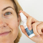 Woman applying 7.6% AHA Leave On Exfoliant skincare product to her face with a white background