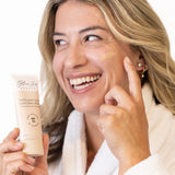 Woman applying Glow jar Beauty tinted SPF sunscreen cream to her face with a tube of sunscreen in hand.