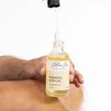 Hand holding a bottle of pineapple body oil with a dropper, on a white background.