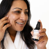 Woman applying glow jar beauty Vitamin C serum product to her face with a bottle of serum in hand.