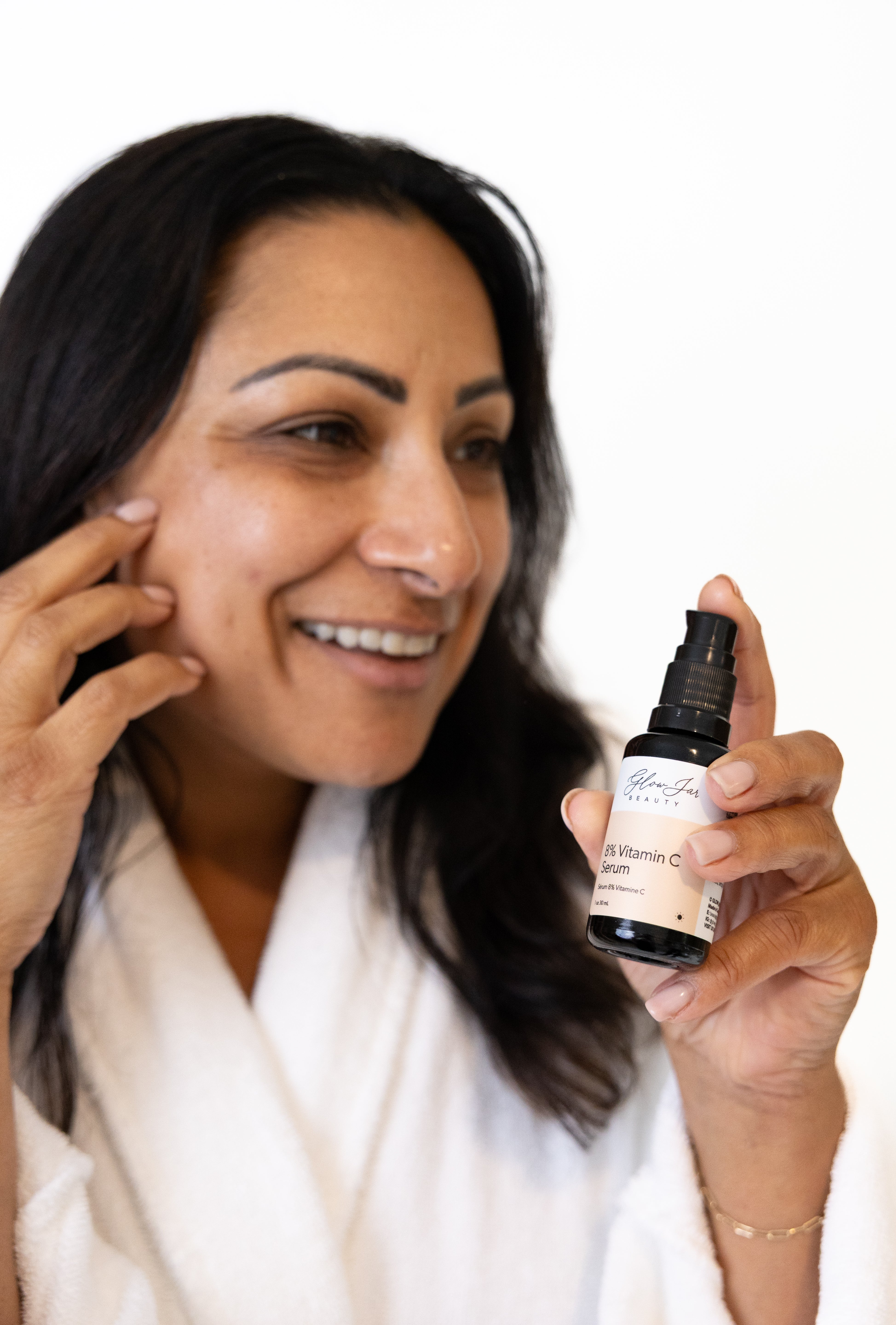 Woman applying glow jar beauty Vitamin C serum product to her face with a bottle of serum in hand.