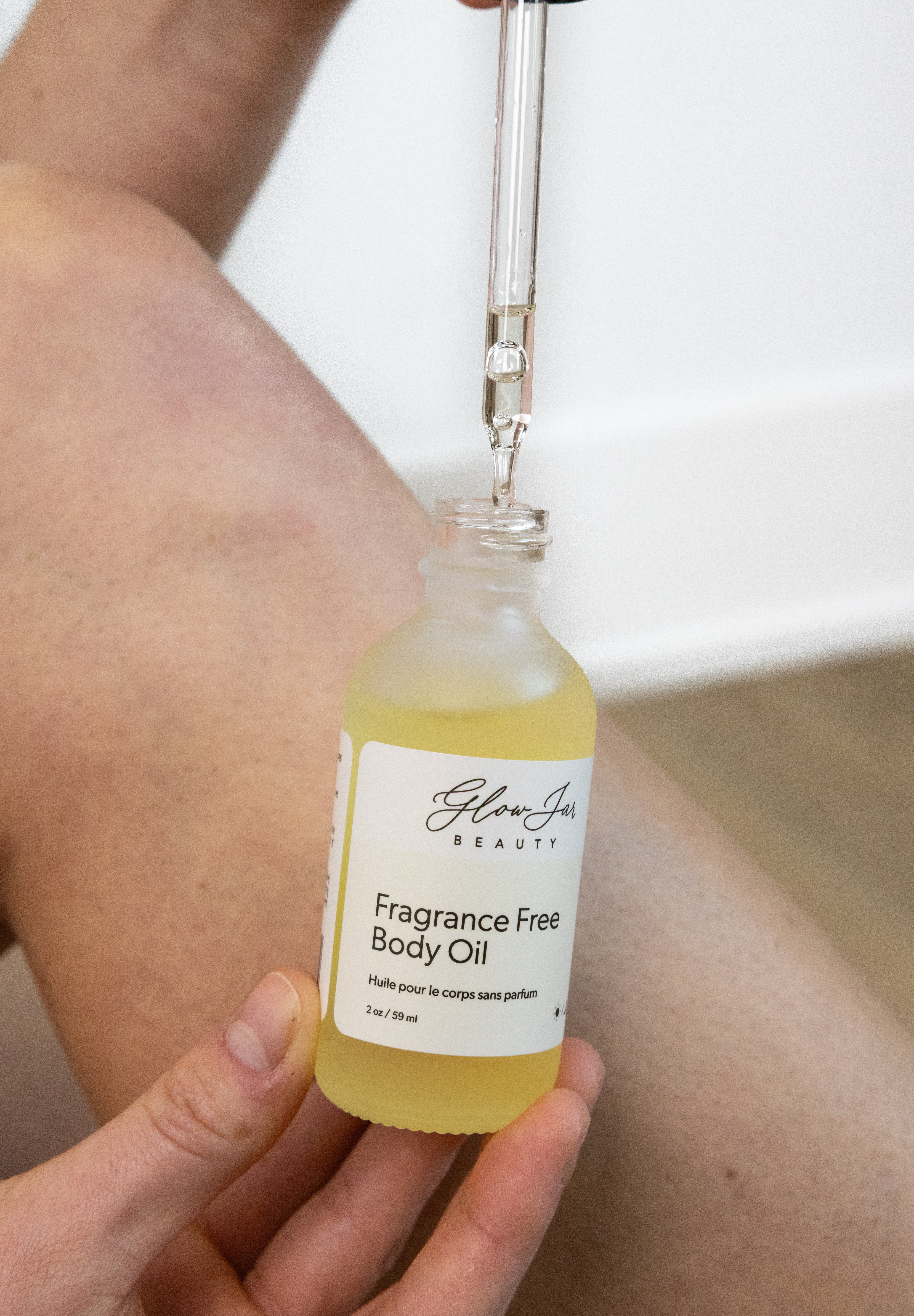 Bottle of Glow Jar Beauty Fragrance Free Body Oil being applied to skin.