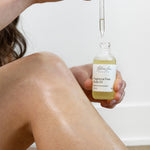 Person applying a bottle of Glow Jar Beauty fragrance-free body oil to their leg.