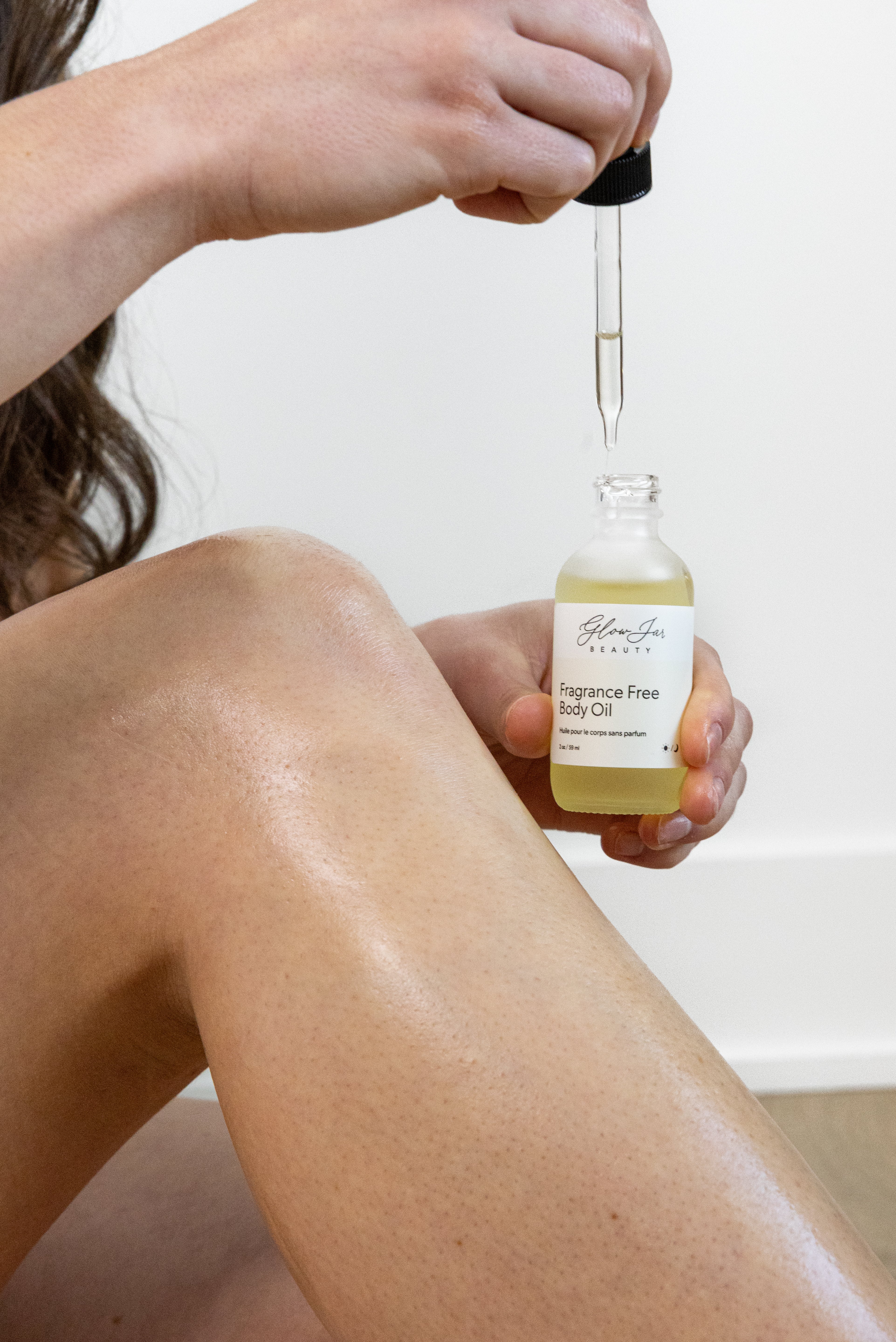 Person applying a bottle of Glow Jar Beauty fragrance-free body oil to their leg.